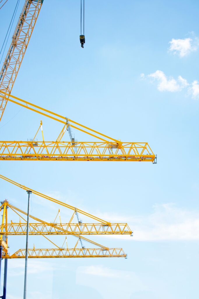 pexels-photo-17297091-17297091 Yellow tower cranes in a construction site reaching into a clear blue sky, symbolizing modern industry.